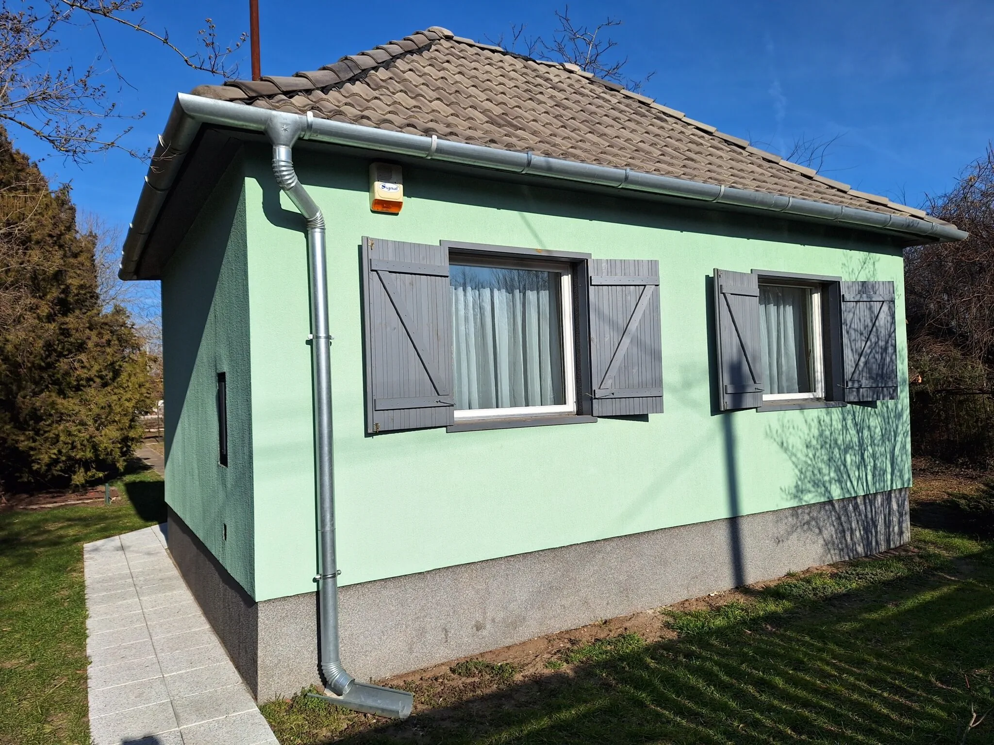 A menta-zöld apartmanház sötétszürke fatáblás ablakokkal
